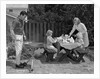1960s man on patio grilling steak with 2 daughters seated at picnic table & wife standing serving food by Anonymous
