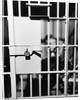 1960s man seated on bench in jail cell with head in hand looking downward by Anonymous