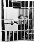 1960s man seated on bench in jail cell with head in hand looking downward by Anonymous