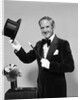 1970s smiling man magician wearing velvet tuxedo white gloves pointing magic wand at top hat looking at camera by Anonymous