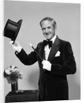 1970s smiling man magician wearing velvet tuxedo white gloves pointing magic wand at top hat looking at camera by Anonymous