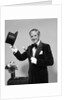 1970s smiling man magician wearing velvet tuxedo white gloves pointing magic wand at top hat looking at camera by Corbis