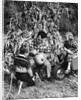 1950s boy & girl sitting in front of corn stalks watching father carve pumpkin by Anonymous