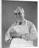 1940s man wearing white apron writing order on pad with pencil looking at camera by Anonymous