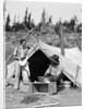 1930s smiling talking couple working by rustic western campsite tent man in cowboy hat smoking pipe washing skillet woman drying dishes by Anonymous
