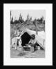 1930s smiling talking couple working by rustic western campsite tent man in cowboy hat smoking pipe washing skillet woman drying dishes by Anonymous