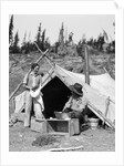 1930s smiling talking couple working by rustic western campsite tent man in cowboy hat smoking pipe washing skillet woman drying dishes by Anonymous