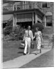 1930s couple walking out of house down sidewalk carrying picnic baskets & thermos jug by Anonymous