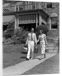 1930s couple walking out of house down sidewalk carrying picnic baskets & thermos jug by Anonymous