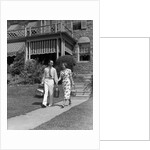 1930s couple walking out of house down sidewalk carrying picnic baskets & thermos jug by Anonymous