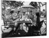 1930s three women and one man sitting at tropical pool side table talking together by Anonymous
