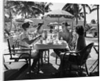 1930s three women and one man sitting at tropical pool side table talking together by Anonymous