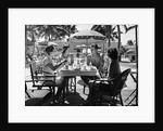 1930s three women and one man sitting at tropical pool side table talking together by Anonymous