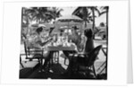 1930s three women and one man sitting at tropical pool side table talking together by Anonymous