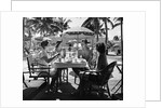 1930s three women and one man sitting at tropical pool side table talking together by Anonymous