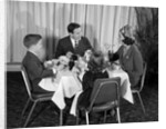 1960s smiling happy family of four eating meal in restaurant dad talking to mom who is wearing turban style hat by Anonymous