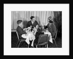 1960s smiling happy family of four eating meal in restaurant dad talking to mom who is wearing turban style hat by Anonymous
