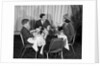 1960s smiling happy family of four eating meal in restaurant dad talking to mom who is wearing turban style hat by Anonymous