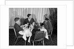 1960s smiling happy family of four eating meal in restaurant dad talking to mom who is wearing turban style hat by Anonymous