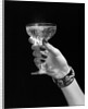 1930s 1940s 1950s woman hand ornate metal bracelet holding up new year toast glass of champagne against black background by Anonymous