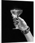 1930s 1940s 1950s woman hand ornate metal bracelet holding up new year toast glass of champagne against black background by Anonymous