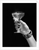1930s 1940s 1950s woman hand ornate metal bracelet holding up new year toast glass of champagne against black background by Anonymous