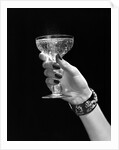1930s 1940s 1950s woman hand ornate metal bracelet holding up new year toast glass of champagne against black background by Anonymous