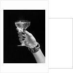 1930s 1940s 1950s woman hand ornate metal bracelet holding up new year toast glass of champagne against black background by Anonymous
