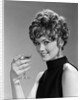 1960s glamorous woman with curly hair and dangling earrings smiling holding a champagne glass looking at camera by Anonymous