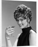 1960s glamorous woman with curly hair and dangling earrings smiling holding a champagne glass looking at camera by Anonymous
