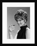 1960s glamorous woman with curly hair and dangling earrings smiling holding a champagne glass looking at camera by Anonymous