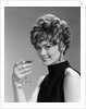 1960s glamorous woman with curly hair and dangling earrings smiling holding a champagne glass looking at camera by Anonymous