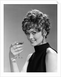 1960s glamorous woman with curly hair and dangling earrings smiling holding a champagne glass looking at camera by Anonymous