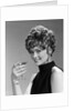 1960s glamorous woman with curly hair and dangling earrings smiling holding a champagne glass looking at camera by Anonymous