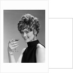 1960s glamorous woman with curly hair and dangling earrings smiling holding a champagne glass looking at camera by Anonymous