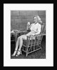 1940s blonde woman in bamboo chair holding up glass of milk smiling wearing white shorts looking at camera by Anonymous
