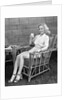 1940s blonde woman in bamboo chair holding up glass of milk smiling wearing white shorts looking at camera by Anonymous