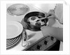 1940s 1950s woman hands frying eggs in iron skillet on electric stove salt and pepper shakers by Anonymous