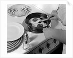 1940s 1950s woman hands frying eggs in iron skillet on electric stove salt and pepper shakers by Anonymous