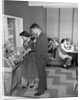 1950s teen couple playing juke box in malt shop with other teens in booths by Anonymous