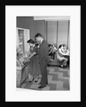 1950s teen couple playing juke box in malt shop with other teens in booths by Anonymous