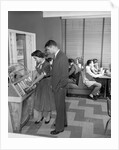 1950s teen couple playing juke box in malt shop with other teens in booths by Anonymous