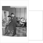 1950s teen couple playing juke box in malt shop with other teens in booths by Anonymous