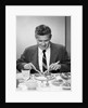 1950s smiling man in suit and tie sitting at table holding knife and fork eating dinner by Anonymous