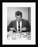 1950s smiling man in suit and tie sitting at table holding knife and fork eating dinner by Anonymous