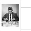 1950s smiling man in suit and tie sitting at table holding knife and fork eating dinner by Anonymous