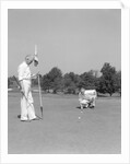 1930s 1940s elderly men on golf green one holding flag the other kneels lining up his putt by Anonymous