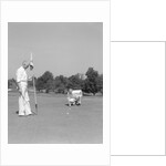 1930s 1940s elderly men on golf green one holding flag the other kneels lining up his putt by Anonymous