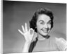 1950s woman smiling wearing pearl necklace looking at camera making okay gesture with hand by Anonymous