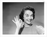 1950s woman smiling wearing pearl necklace looking at camera making okay gesture with hand by Anonymous